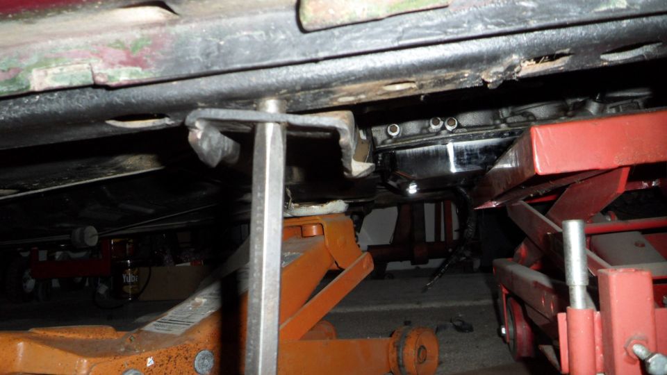 Underside of a vehicle supported by jacks, showing transmission pan and frame.