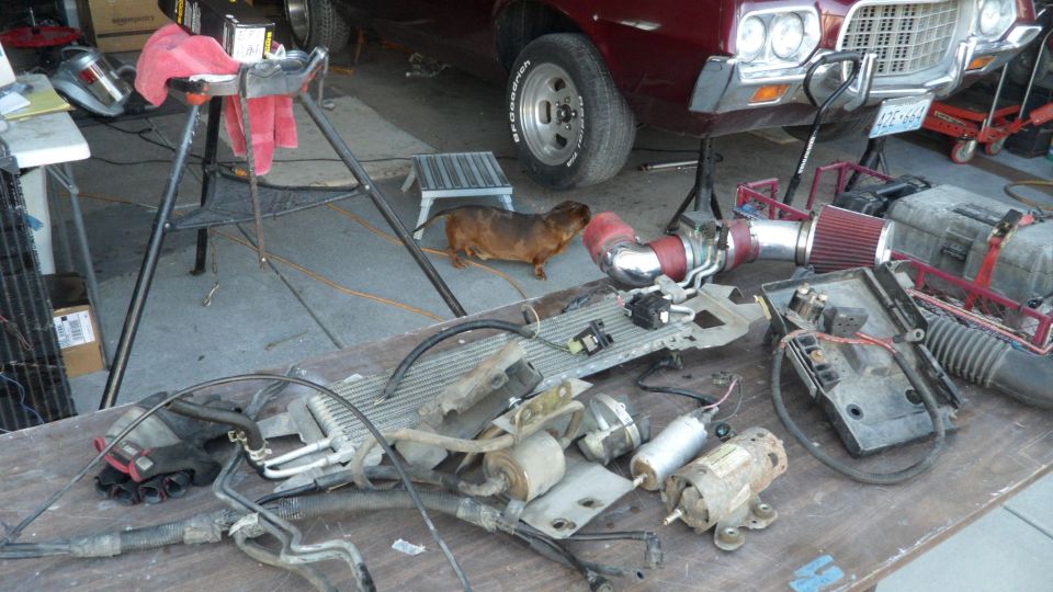 Car parts laid out on a table in front of a classic car.