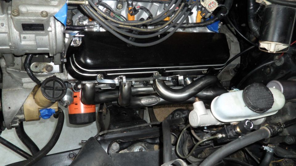 Close-up of engine bay with JBA exhaust headers, black valve cover, and brake fluid reservoir.
