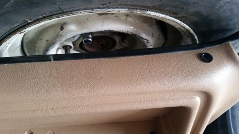 1985 Ford Bronco - Underbody view of a spare tire on a white steel wheel and retainer beneath a tan interior trim panel.