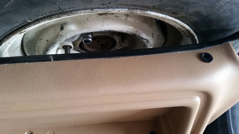 Underbody spare tire mounted on white steel wheel beneath tan vehicle trim panel