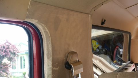 1985 Ford Bronco - Interior view of a vehicle's rear passenger side, showing the window frame, a seatbelt buckle, and the headliner. The exterior scene visibl…