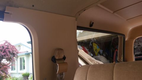 1985 Ford Bronco - Interior view of a tan SUV, likely a 1985 Ford Bronco, showing the ceiling, a portion of the rear window, and a seatbelt mechanism. Outside…