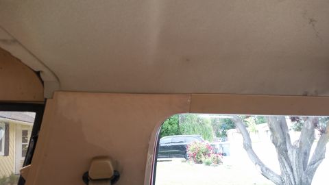 1985 Ford Bronco - Interior view of a vehicle's headliner and side panel, showing a custom wood trim installation above a window opening. Outside, a house and…