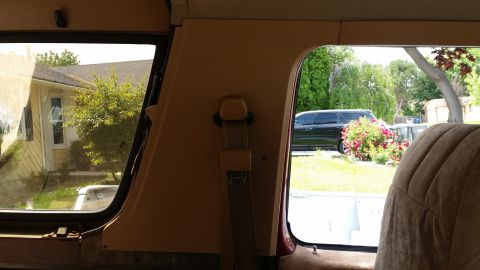 1985 Ford Bronco - Interior view of a vintage vehicle, showing a tan seatbelt mechanism and a portion of the interior trim. Outside the window, a residential…