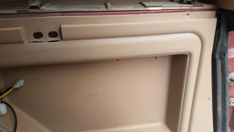 1985 Ford Bronco - This is a close-up interior shot of a tan door panel, likely from a 1985 Ford Bronco. Visible details include two oval-shaped cutouts, wiri…