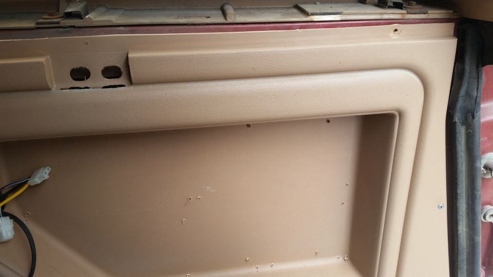 Tan interior door panel with cutouts and wiring.