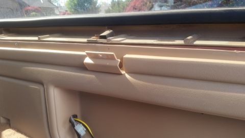 1985 Ford Bronco - Close-up view of the interior dashboard trim and wiring harness of a vehicle. A beige plastic trim piece is visible, along with a metal bra…