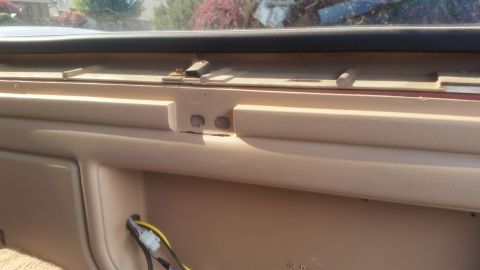 1985 Ford Bronco - This is a close-up interior shot of a tan dashboard area, likely from a vintage SUV, showing two circular cutouts and some wiring harness.