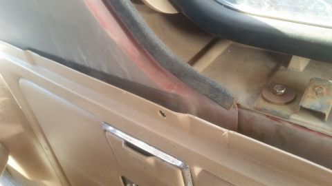 1985 Ford Bronco - A close-up view of the interior door panel and window seal of a vintage vehicle, showing tan trim and a black rubber seal along the window…