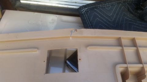 1985 Ford Bronco - A close-up view of a tan plastic lid with a rectangular cutout and a small metal clip attached to the edge. The lid appears to be part of a…