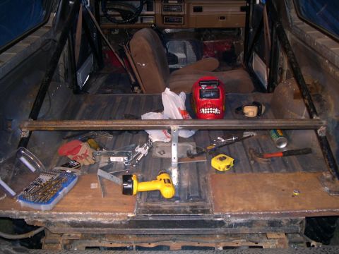 1986 Ford Bronco - The interior of a vehicle shows a roll cage installation with various tools scattered around.
