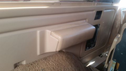 1985 Ford Bronco - The interior of a vintage Ford Bronco shows a tan door panel with a molded armrest and a speaker grille cutout. The textured carpeted floor…