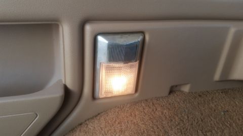 1985 Ford Bronco - A close-up interior shot shows a lit dome light mounted in the tan plastic trim of a vehicle. The light illuminates the brown carpeted floo…