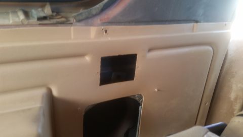 1985 Ford Bronco - The interior of a vehicle shows a tan door panel with a rectangular cutout. Another larger opening is visible below the cutout, revealing d…