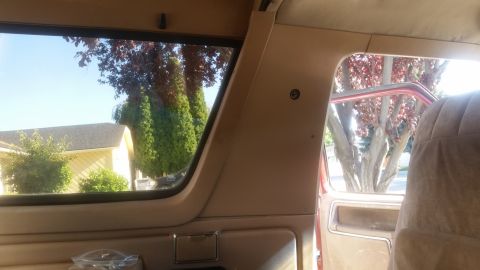 1985 Ford Bronco - Interior view of a vintage Ford Bronco looking out the passenger side window. The view shows a residential area with trees and a yellow hou…