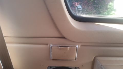 1985 Ford Bronco - This is a close-up interior shot of a tan door panel with a small, flip-top ashtray and a portion of the window visible. The window shows a…