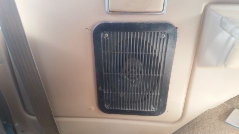 1985 Ford Bronco - A close-up view of a black speaker grille with vertical slats, mounted on a tan interior panel. The grille is secured with four visible scr…