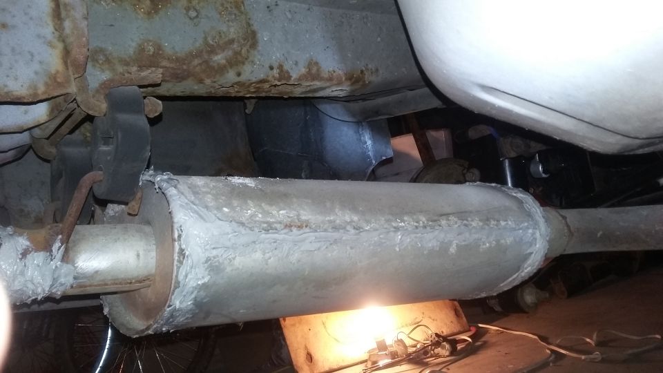 Underside of a car showing a repaired muffler and rusted frame.