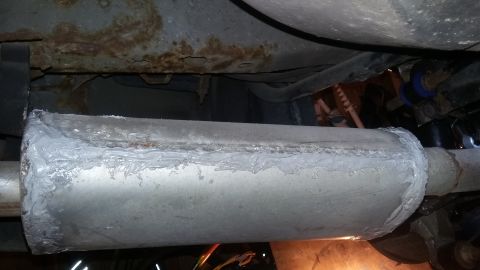 2000 Pontiac Grand Prix - A section of a car's exhaust system, specifically a muffler, has been repaired with a grey sealant. The underside of the vehicle's chassis,…