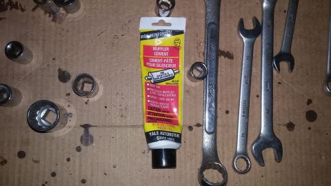 2000 Pontiac Grand Prix - A tube of muffler cement is surrounded by various automotive tools including socket wrenches and open-end wrenches, laid out on a cardboard…