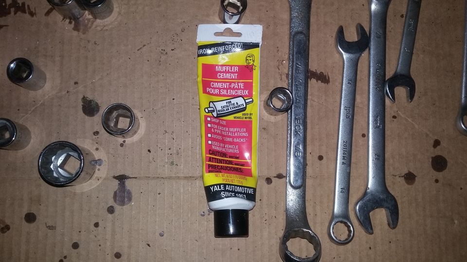 Tube of muffler cement with automotive tools on cardboard.