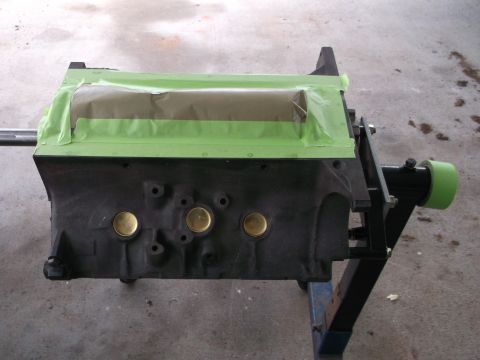 1969 Ford Mustang - A black engine block is prepared for painting with masking tape covering the top section.