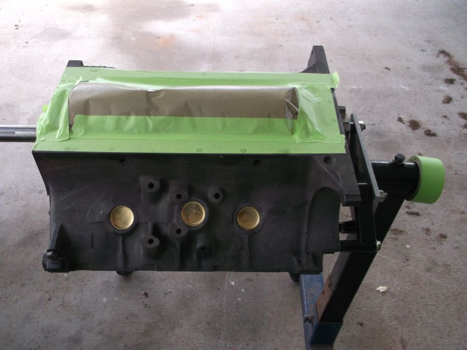 Black engine block with green and tan masking tape on top, mounted on a stand