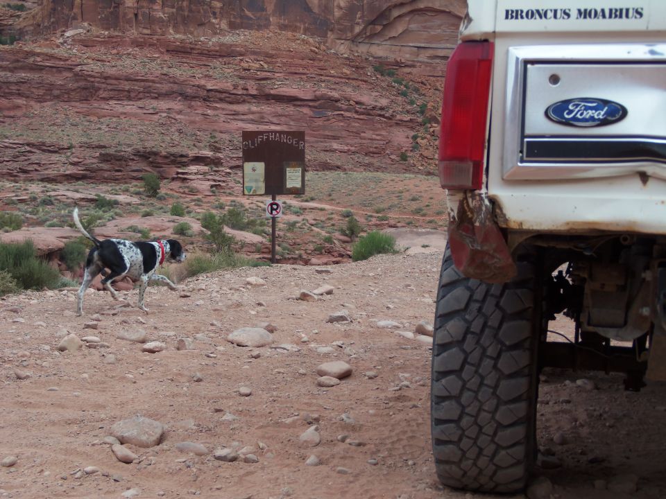 Rear view of a white 1984 Ford Bronco parked on a dirt road near a sign