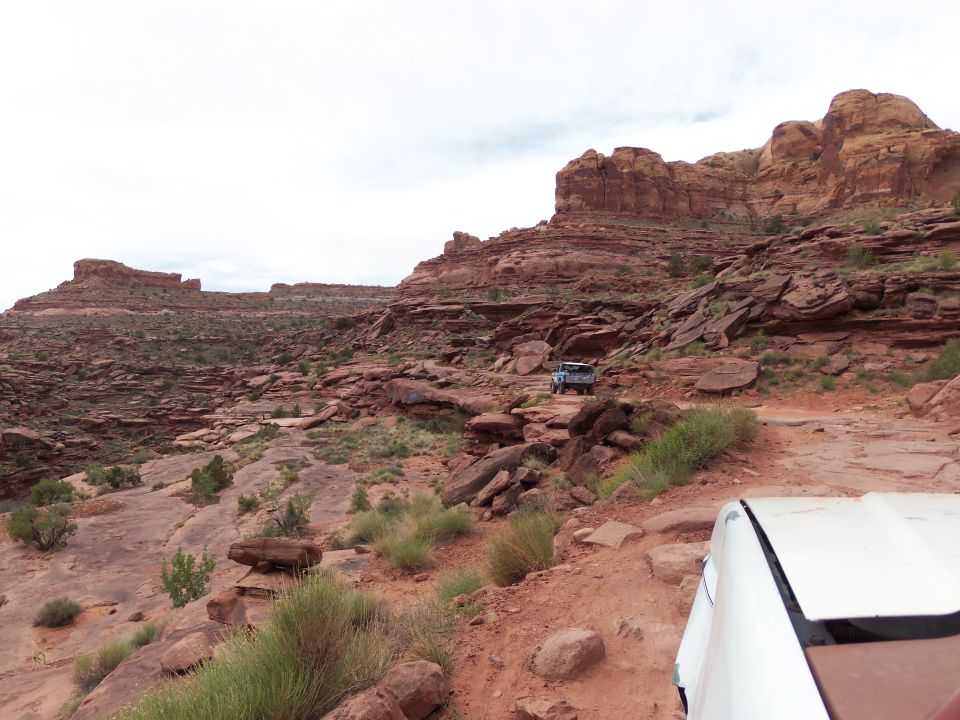 Two SUVs on a rocky off-road trail in a desert landscape with red rock formations