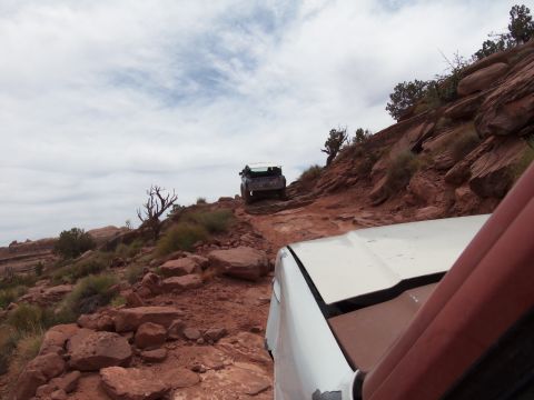 1984 Ford Bronco - Two off-road vehicles navigate a challenging rocky trail under a cloudy sky.