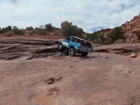 1984 Ford Bronco - This SUV is navigating a challenging rocky terrain under a cloudy sky.
