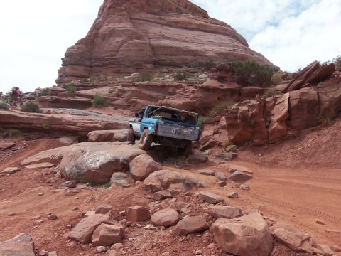 1984 Ford Bronco - A blue pickup truck tackles a challenging rocky trail under a cloudy sky.