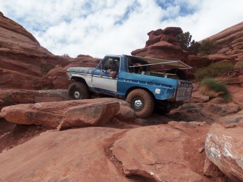 1984 Ford Bronco - This modified Ford Bronco navigates a rocky trail, its off-road capabilities. The text 'Faded Glory' is visible on the door.