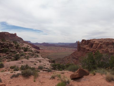 1984 Ford Bronco - A vast desert landscape unfolds with towering red rock formations under a cloudy sky.