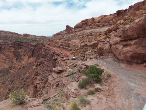 1984 Ford Bronco - A vehicle navigates a treacherous path through a rocky, arid landscape under a cloudy sky.