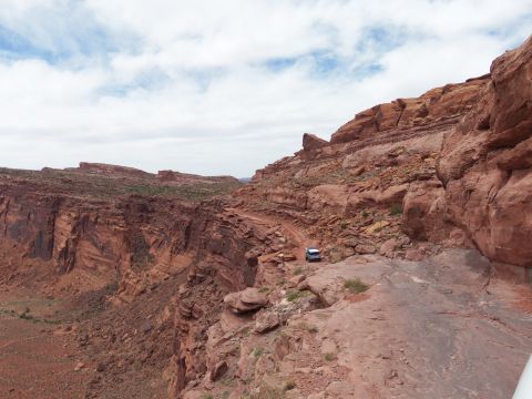 1984 Ford Bronco - A white SUV navigates a precarious dirt road along the edge of a vast desert canyon.