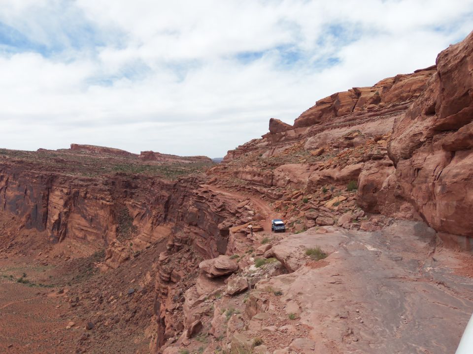 White SUV on a narrow dirt road beside a deep red rock canyon