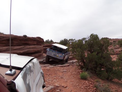 1984 Ford Bronco - An off-road SUV navigates a challenging rocky path, with another vehicle partially visible in the foreground.