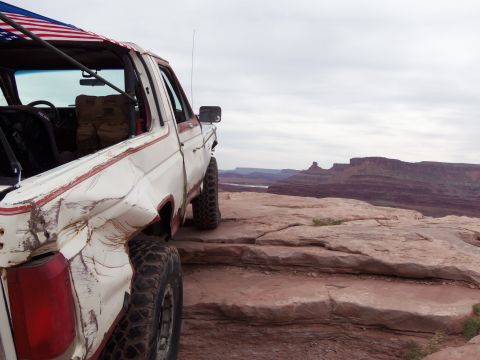 1984 Ford Bronco - This heavily modified Ford Bronco is parked on a cliff edge overlooking a canyon landscape.