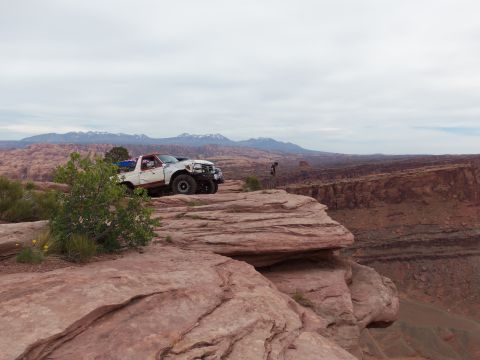 1984 Ford Bronco - A white Ford Bronco with a red top sits precariously on a cliff edge overlooking a canyon.