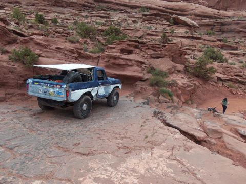 1984 Ford Bronco - A modified Ford Bronco navigates a , rocky desert landscape with a person and dog nearby.