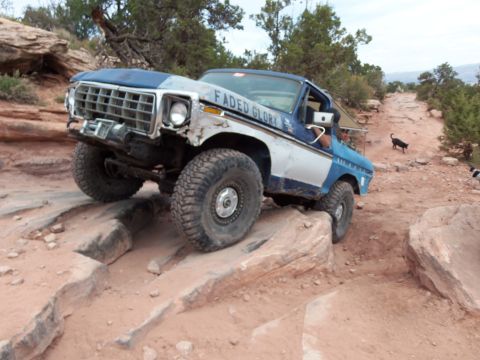1984 Ford Bronco - This modified Ford Bronco is tackling a challenging off-road course with large rocks and steep inclines.