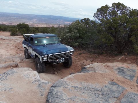 1984 Ford Bronco - A blue and white Ford Bronco tackles a challenging rocky terrain on an off-road adventure.