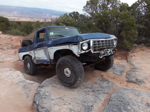 1984 Ford Bronco - This heavily modified Ford Bronco is navigating a rocky trail, showing significant off-road use.