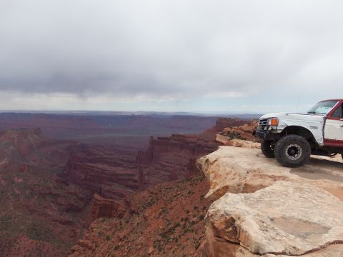 1984 Ford Bronco - A modified truck sits on the edge of a vast canyon under a cloudy sky.