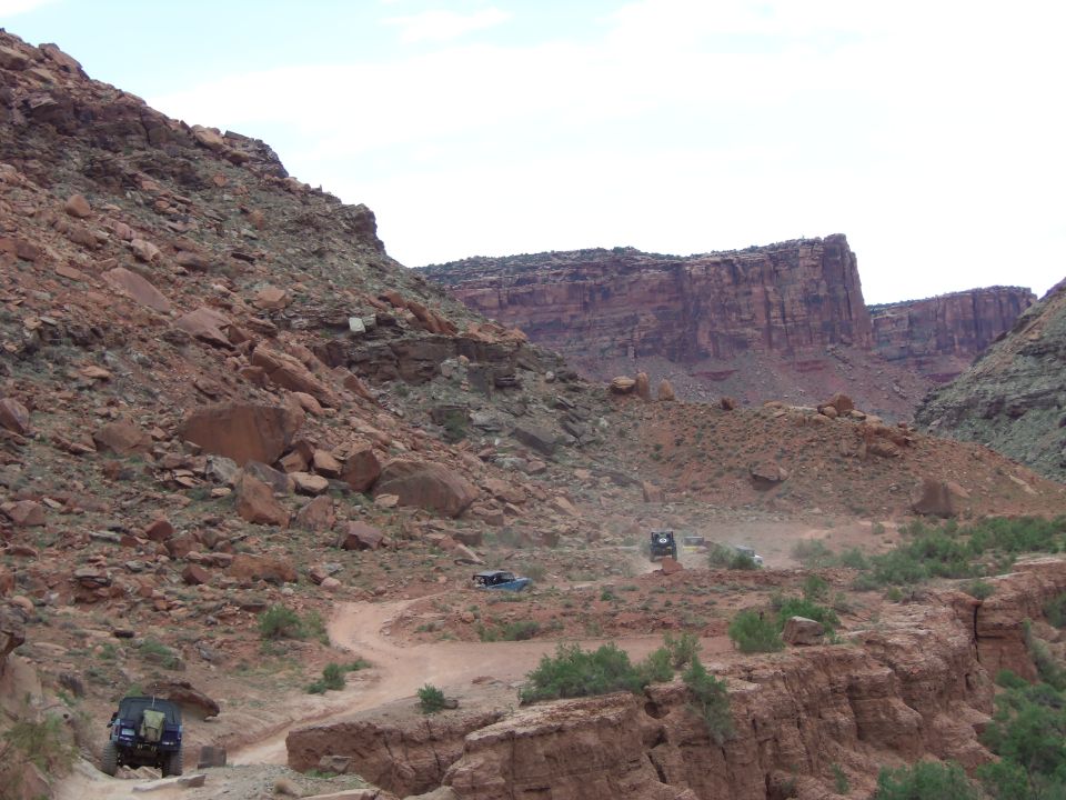 Off-road vehicles navigate a dusty trail through a rocky canyon landscape