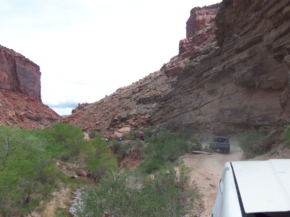 Several off-road vehicles navigate a dusty canyon road