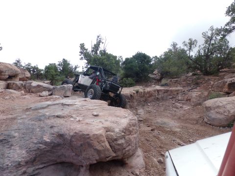 1984 Ford Bronco - An off-road buggy tackles a challenging rocky obstacle, with a portion of another vehicle visible in the foreground.