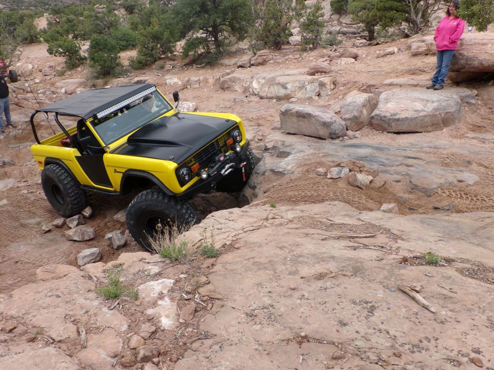 Yellow Ford Bronco with black hood and roof rack, navigating rocky terrain